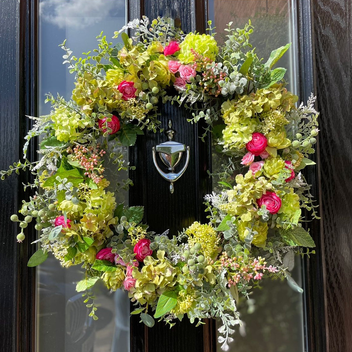 Faux floral wreath with green and pink flowers on a door. UV protected.