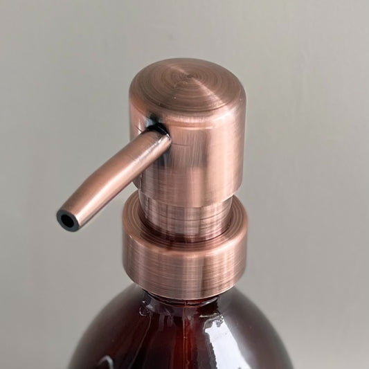 Amber glass refillable bottle with brass-effect pump, styled on a bathroom counter.