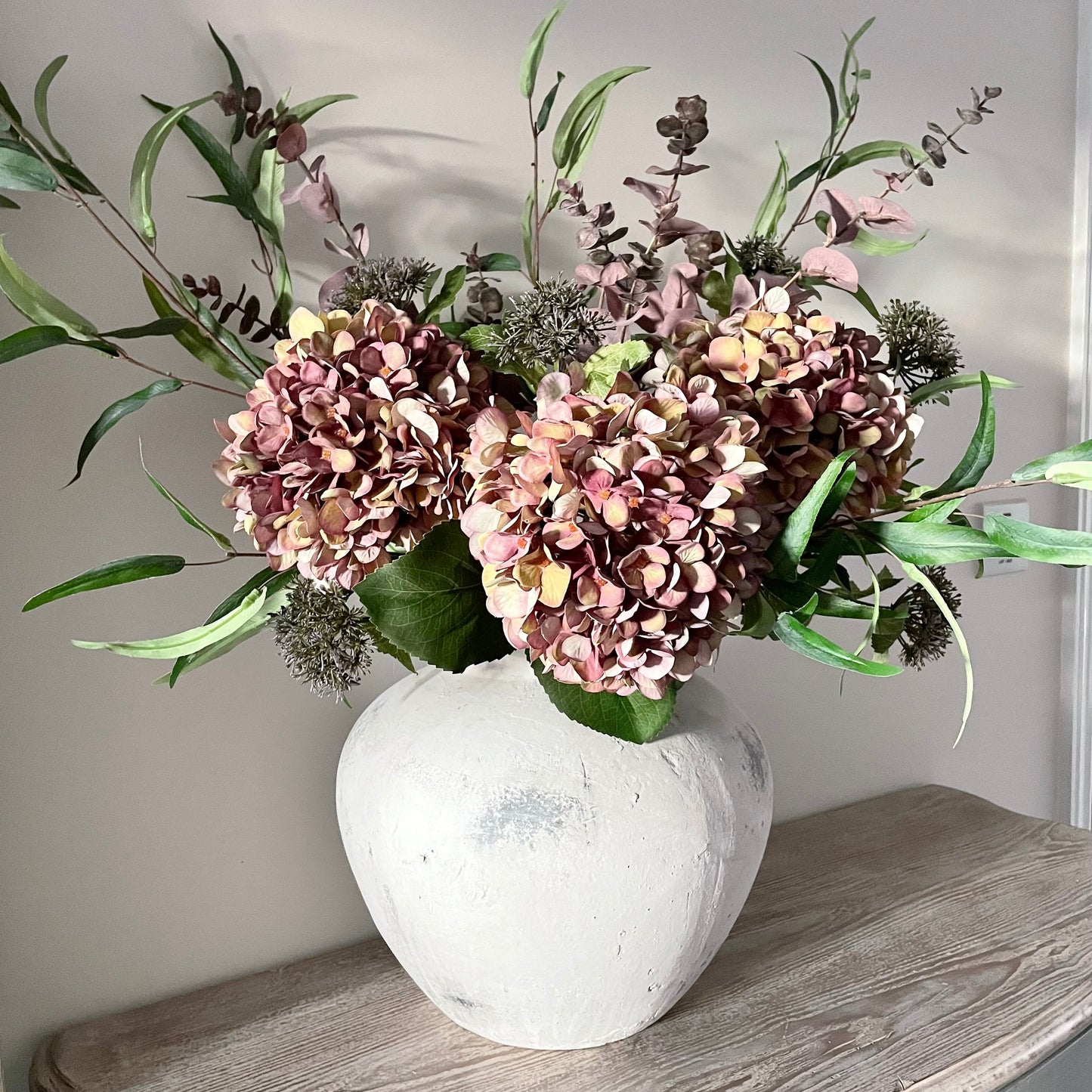 Autumn bouquet of faux flowers in a stone vase on a wooden console table with a neutral background.