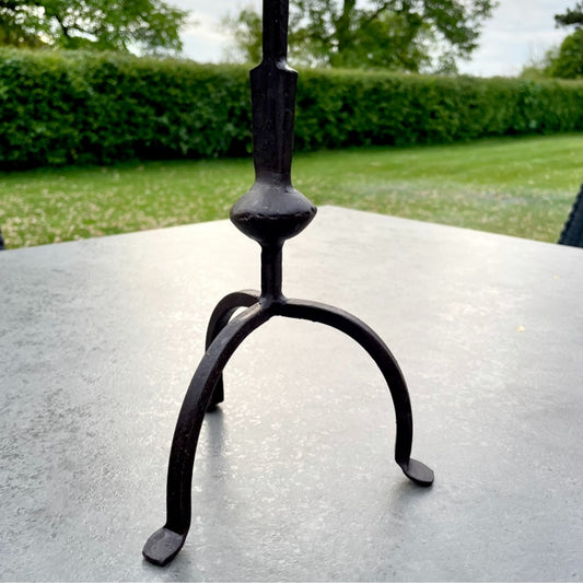 Tall rustic metal candlestick with thin stem and three leg base, styled on a dining table.