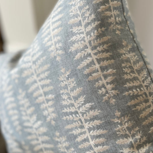 Blue cushion with beige and white leaf print styled on a neutral armchair with a throw.