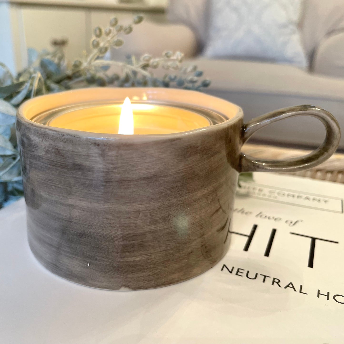 Candle in a rustic black wash ceramic mug, styled on a book.