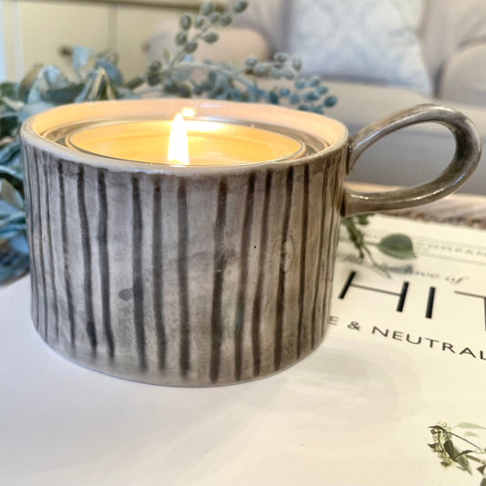 Decorative mug style candle holder on a rattan side table and book.