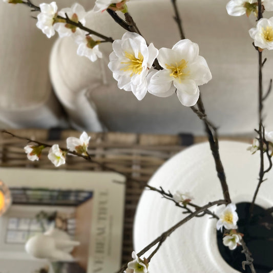 Close up of realistic cherry blossom stem styled in a white ceramic vase.