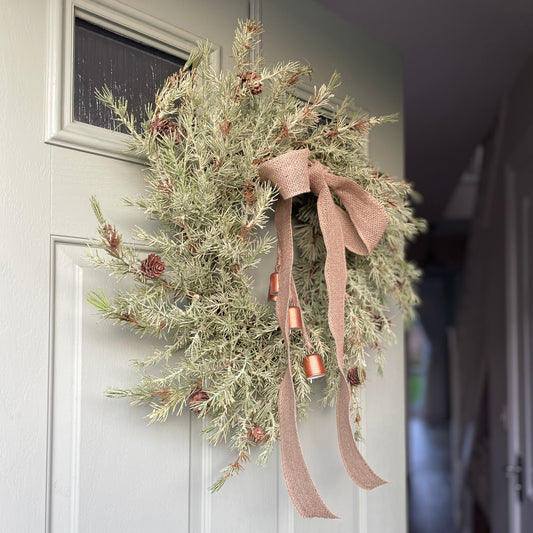 Close up of forest themed Christmas wreath with natural foliage and bells.