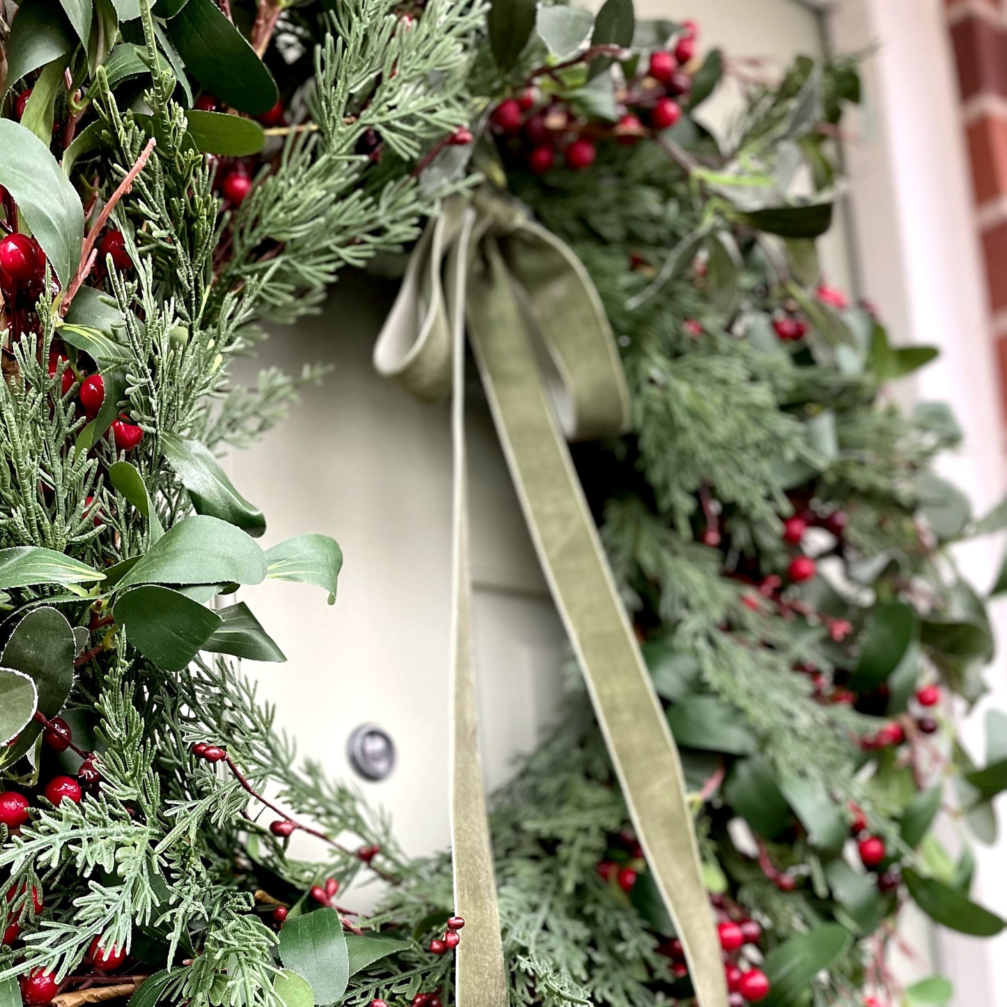 Winter wreath with velvet bow, styled on a green country front door