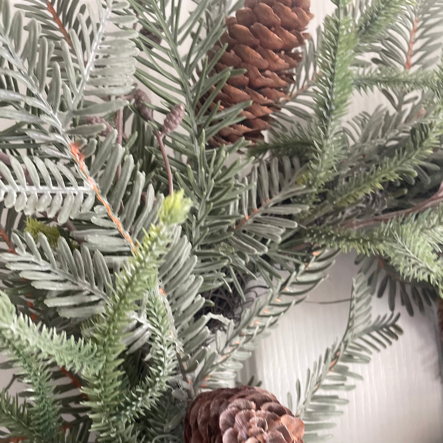 Close up of faux cones and ferns on woodland Christmas wreath. Styled on a white background.