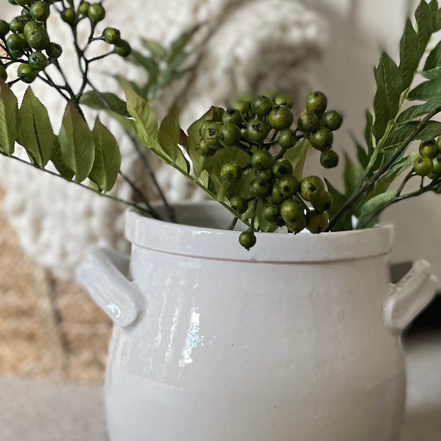 Close up of realistic artificial green berries on stems in a white stone vase.