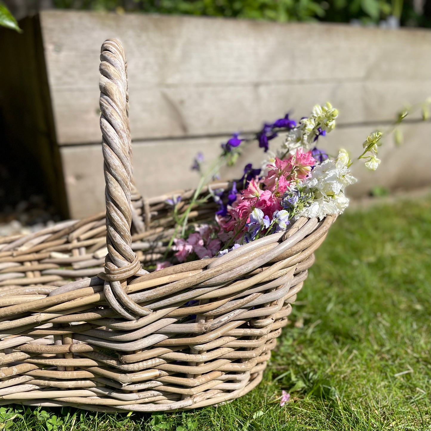 Close up of handwoven rattan flower basket with loop handle, styled with garden flowers.