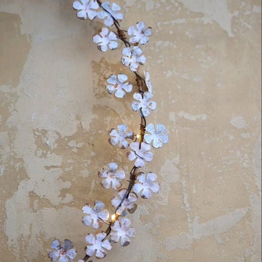 Dainty wildflower wreath with faded white leaves and warm white LED lights, hanging on a rustic wall.