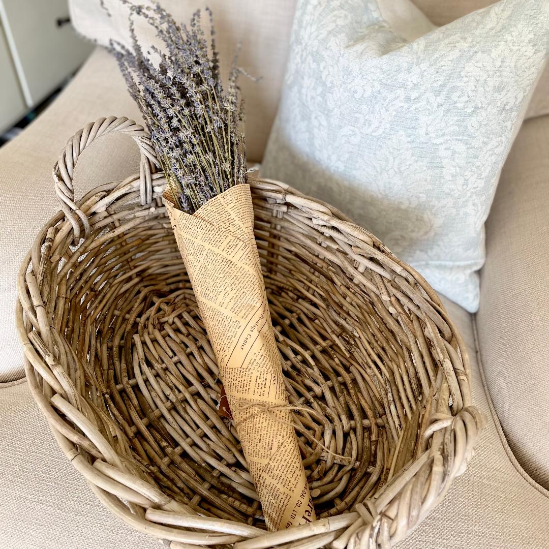 Dried lavender bunch wrapped in brown paper and tied with jute string, styled on a chair in a rattan basket.