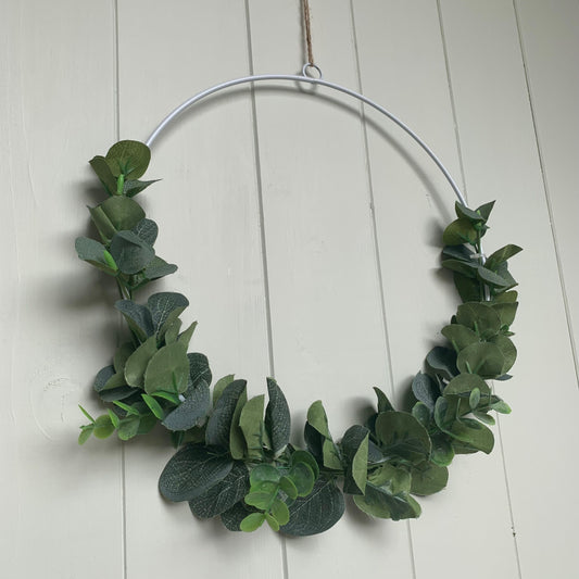 White metal wreath decorated with artificial eucalyptus and hanging on a door with jute string.