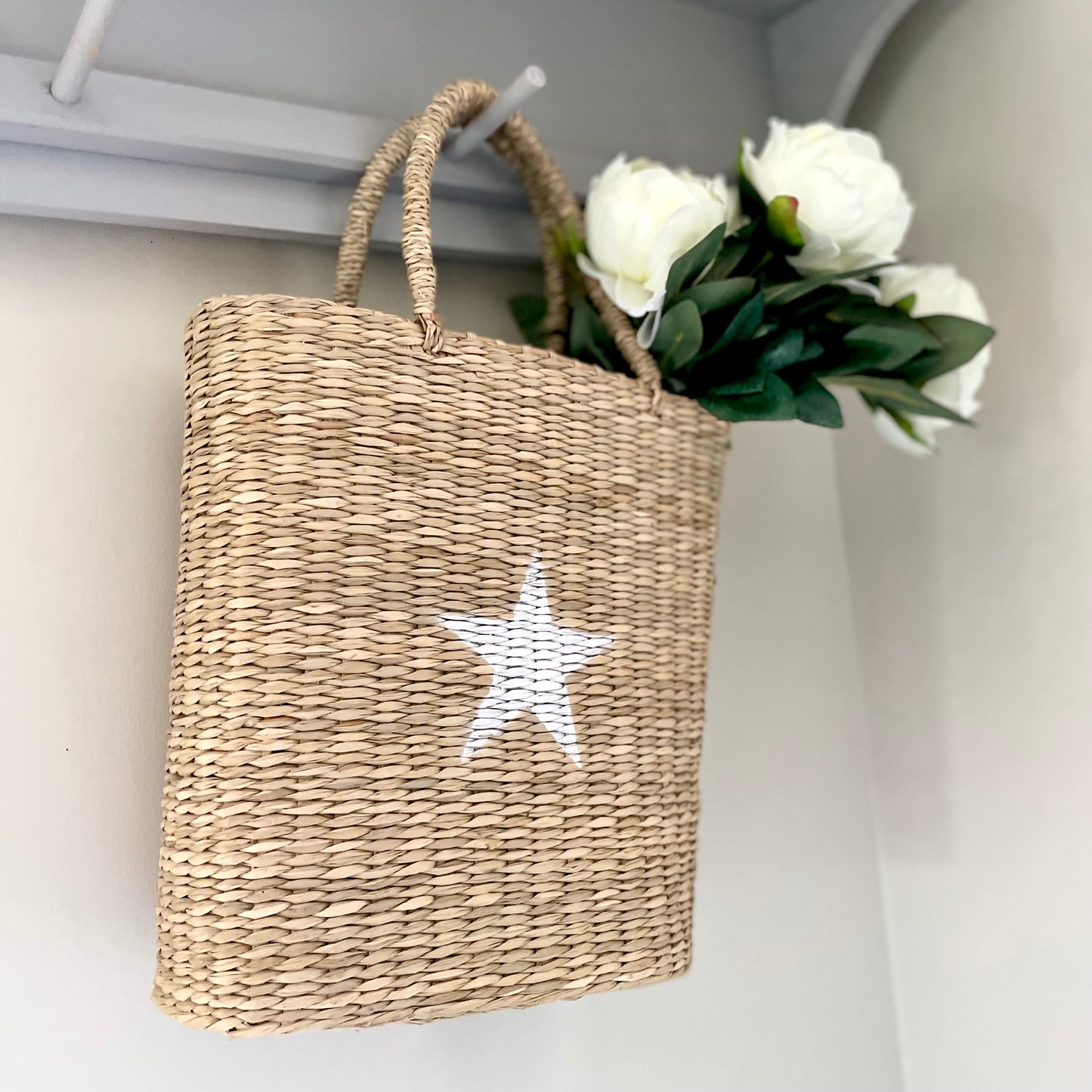 basket of white peony faux stems hanging on a peg shelf.
