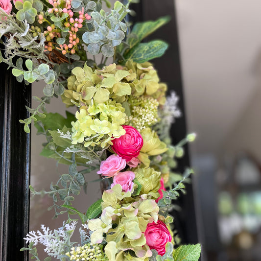 Close up of faux roses, berries and eucalyptus foliage on summer wreath. Styled on a black front door.