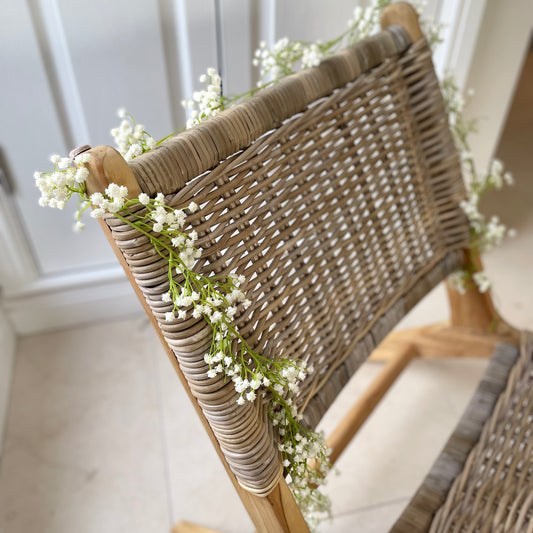 White faux gypsophila faux flower garland draped on a rattan chair.