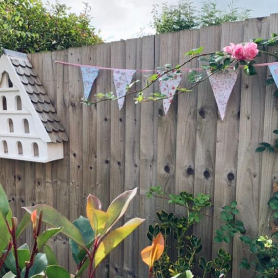 Decorative floral bunting with flowers on a wooden fence in a garden setting.