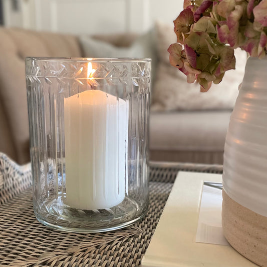 Glass hurricane lantern with leaf etched and ribbed glasswork. Styled on a rattan tray with flowers in a cosy living room