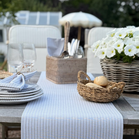 Outdoor table setting with plates, cutlery, and bread on a striped table runner.