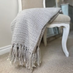 Grey soft textured throw with tassels, draped on a neutral chair.