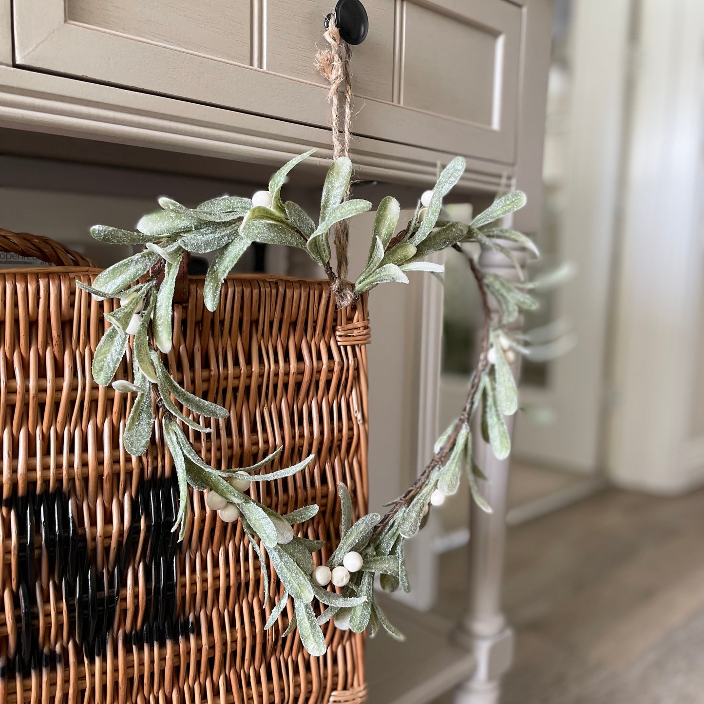 Heart-shaped glittered mistletoe wreath with white berries, styled on a console table with rustic basket.