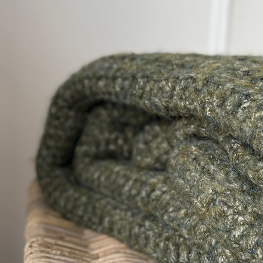 Folded green textured blanket styled on a wicker basket.