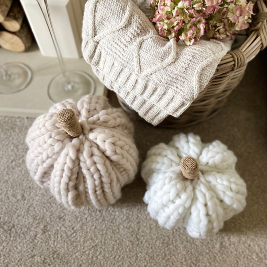 White chunky knitted pumpkin with twine stalk styled next to a rustic basket with cable knit throw.