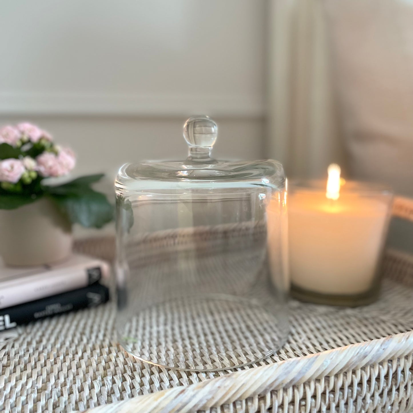 Clear glass cloche dome styled next to a candle on a tray with flowers.