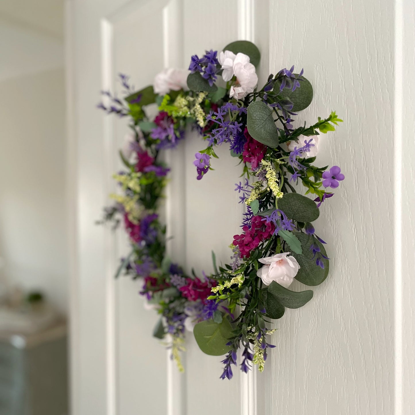 Faux lavender wreath with purple and white blooms, eucalyptus and peach wildflowers, 40 cm diameter styled on a white door.
