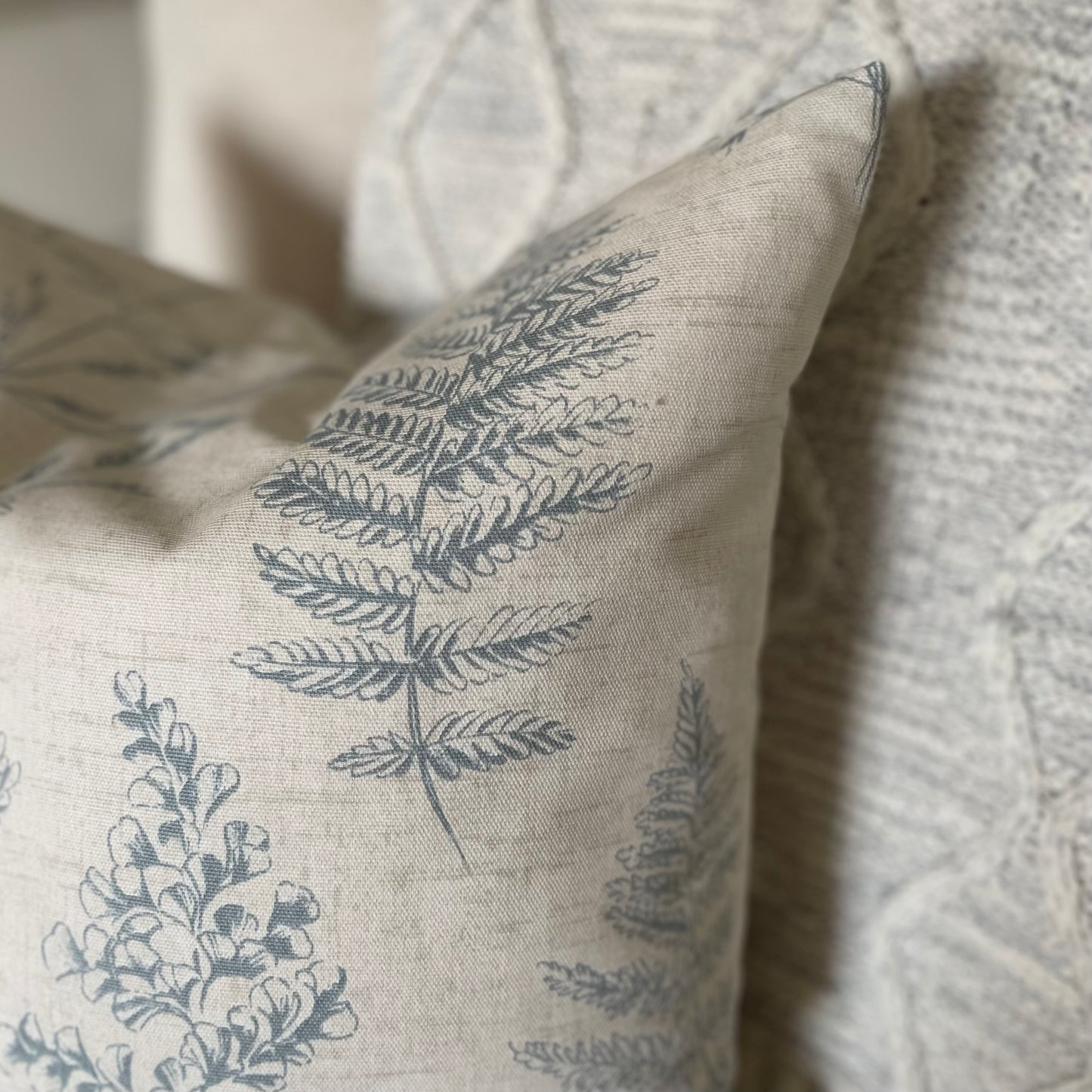 Natural cushion with blue leaf pattern styled on a neutral armchair with a throw.