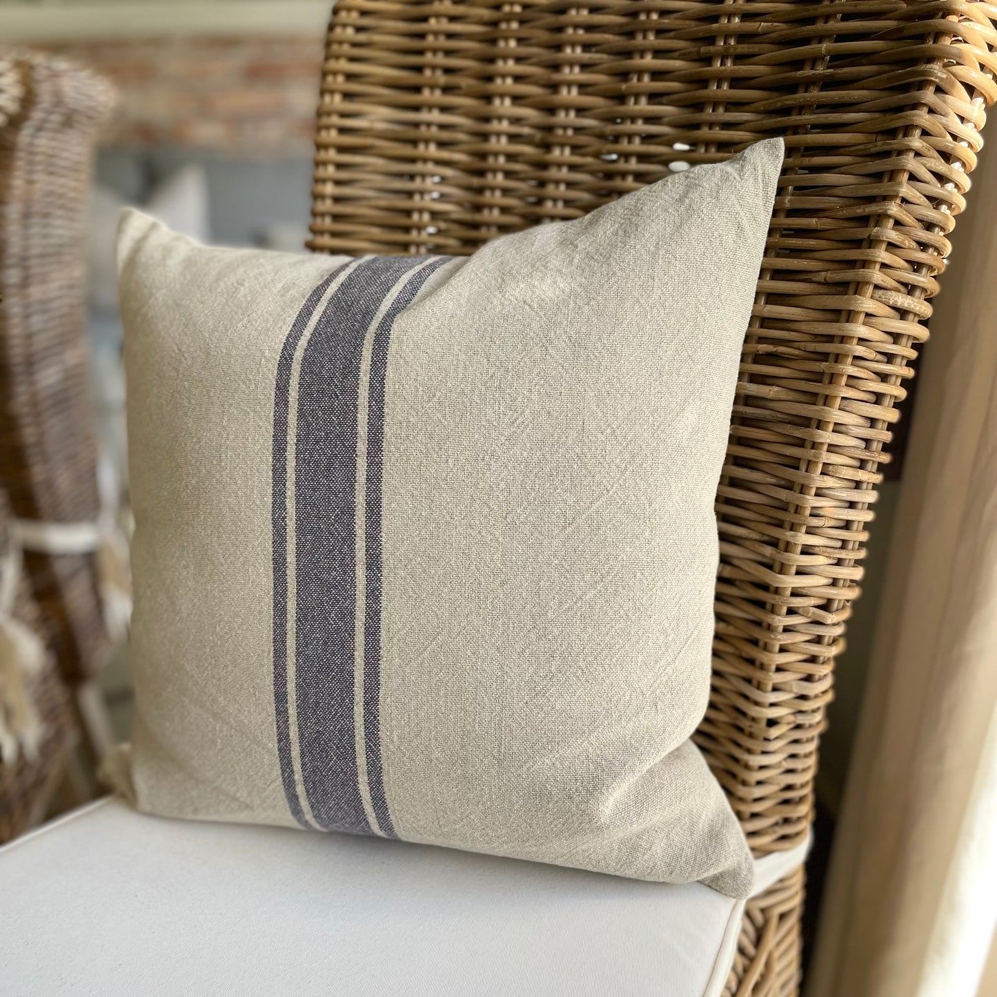 Natural linen cushion with blue grain sack stripe styled on a rustic wooden chair.