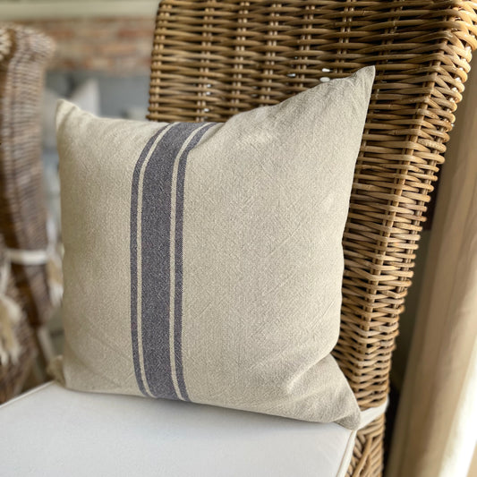Natural linen cushion with blue grain sack stripe styled on a rustic wooden chair.