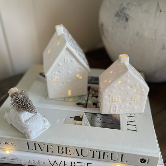 White porcelain tea light house with cut out windows and stars, glowing softly with a lit candle inside.