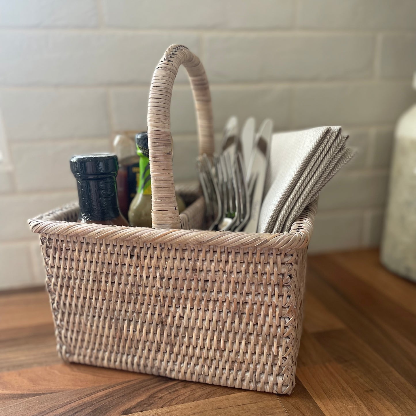 Ethically sourced natural rattan caddy for alfresco dining. Styled on a wooden kitchen worktop.