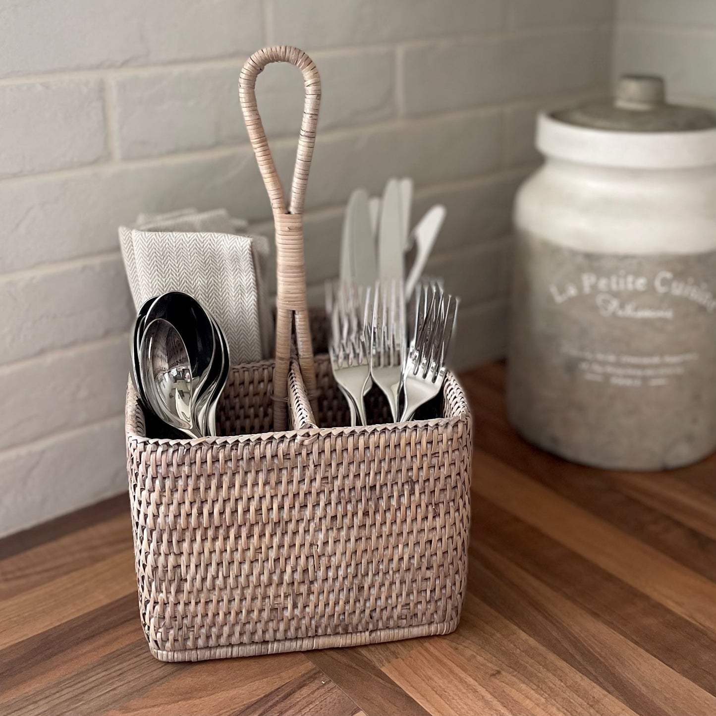 Whitewashed rattan caddy with handle for cutlery or condiments. Styled in a kitchen.