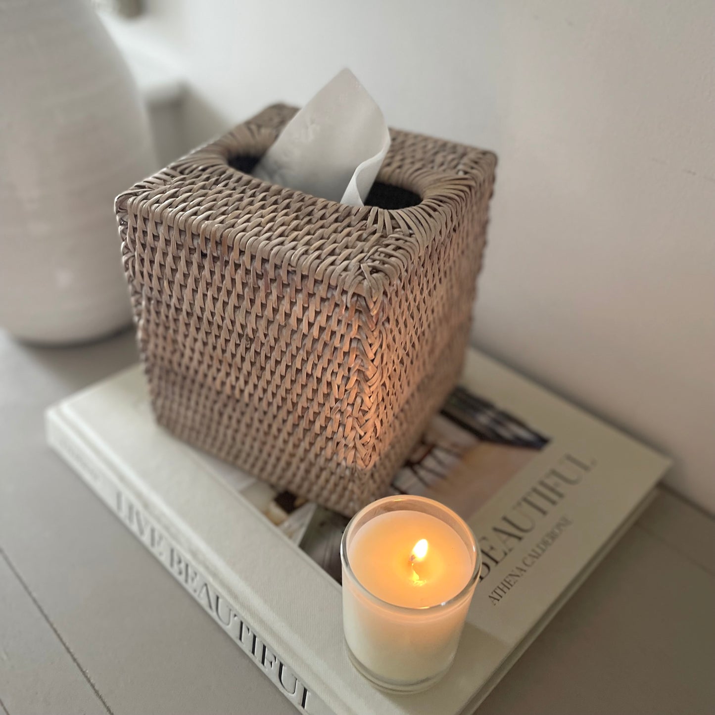 Ethically sourced rattan tissue box cover styled on a console table with boks and a candle.
