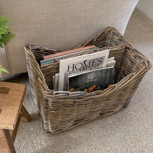 Rattan basket holding magazines and books. Styled on a beige carpet in a living room.