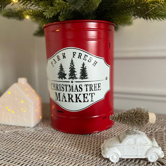 Faux Christmas tree styled in metal tin Styled on a rattan base with a white panelled wall.