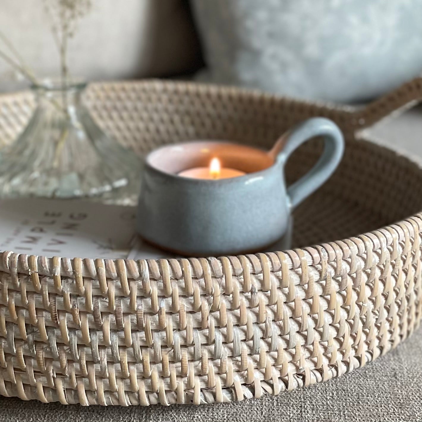 Whitewashed round rattan tray with handles styled on a settee with home accessories.
