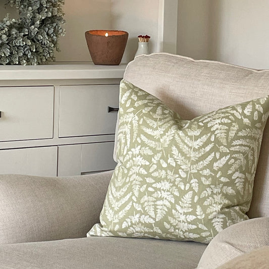 Sage green cushion with fern leaf detailing styled on a neutral armchair with a throw.