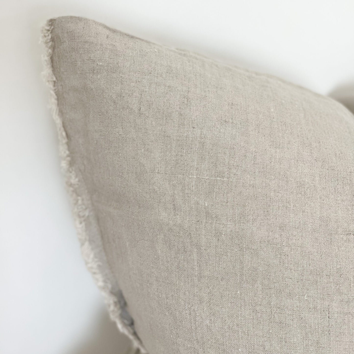Close up of linen sand coloured cushion with frayed edges.