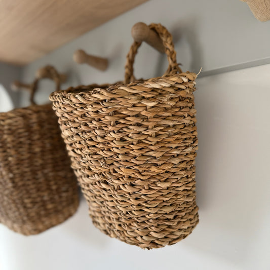Handwoven seagrass hanging baskets with handles, styled on a peg rail and filled with dried flowers for a rustic, natural look.