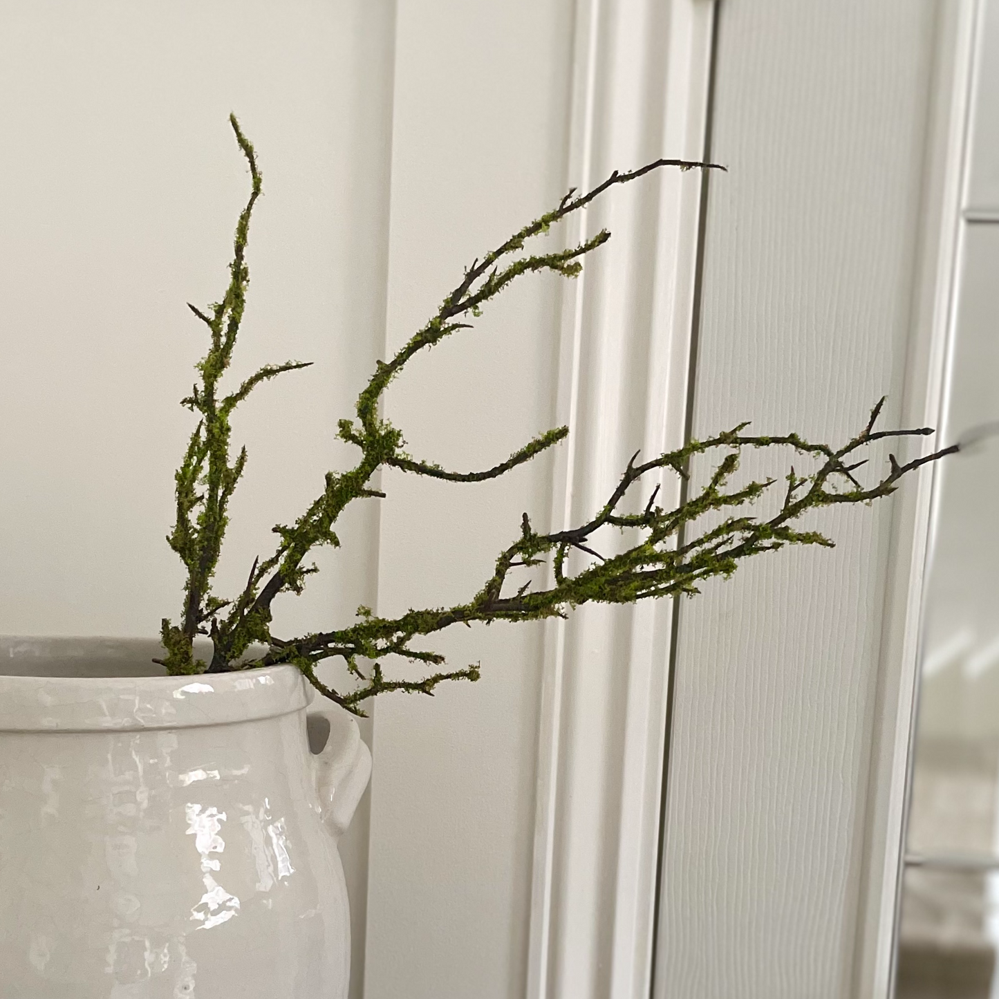 Close up of lifelike moss on decorative branch. Styled in a ceramic glazed pot with handles.