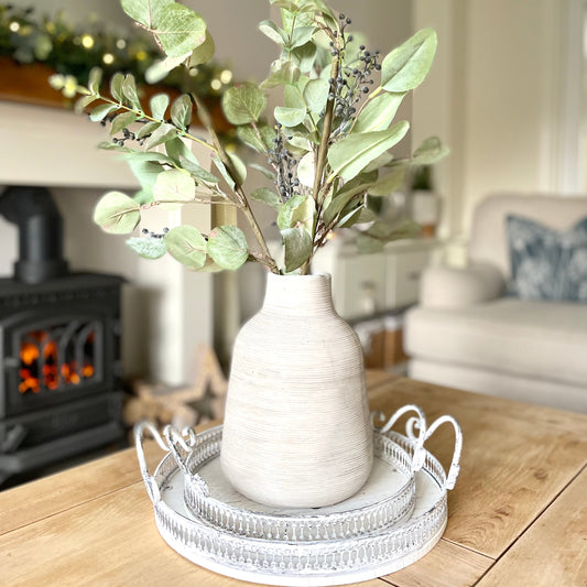 Rustic stone vase with irregular shape and textured earthy finish, styled with natural foliage on a wooden coffee table.