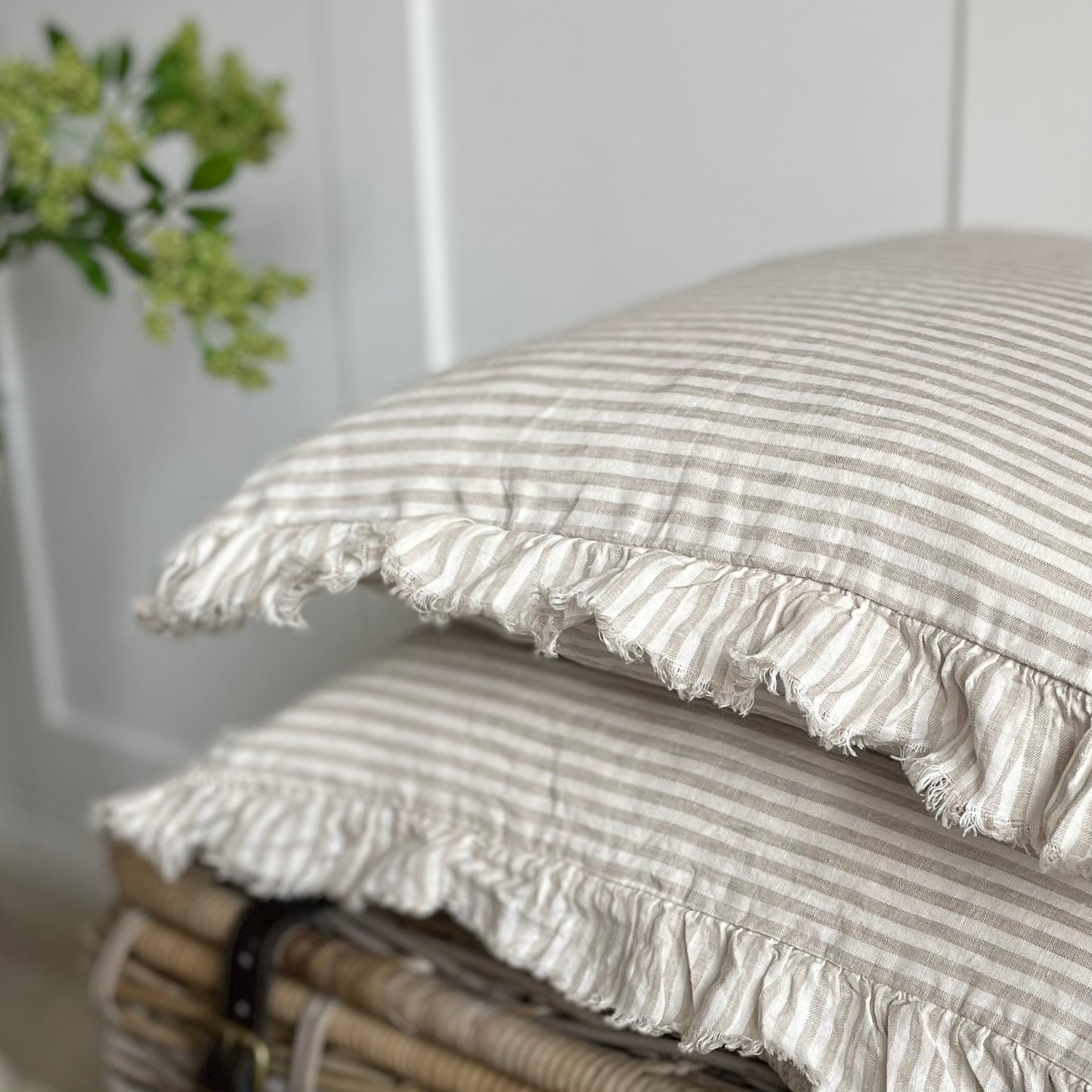 Neutral beige cushion with delicate stripes and ruffled edging, adding timeless charm to a cosy living space.