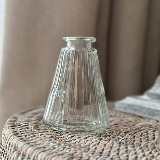 Clear glass bud vase on a woven surface with a neutral background