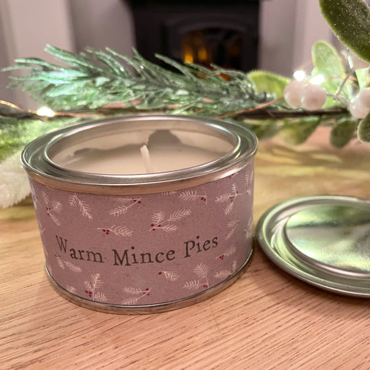 Warm mince pies scented tin candle styled on a wooden coffee table with a christmas faux garland.