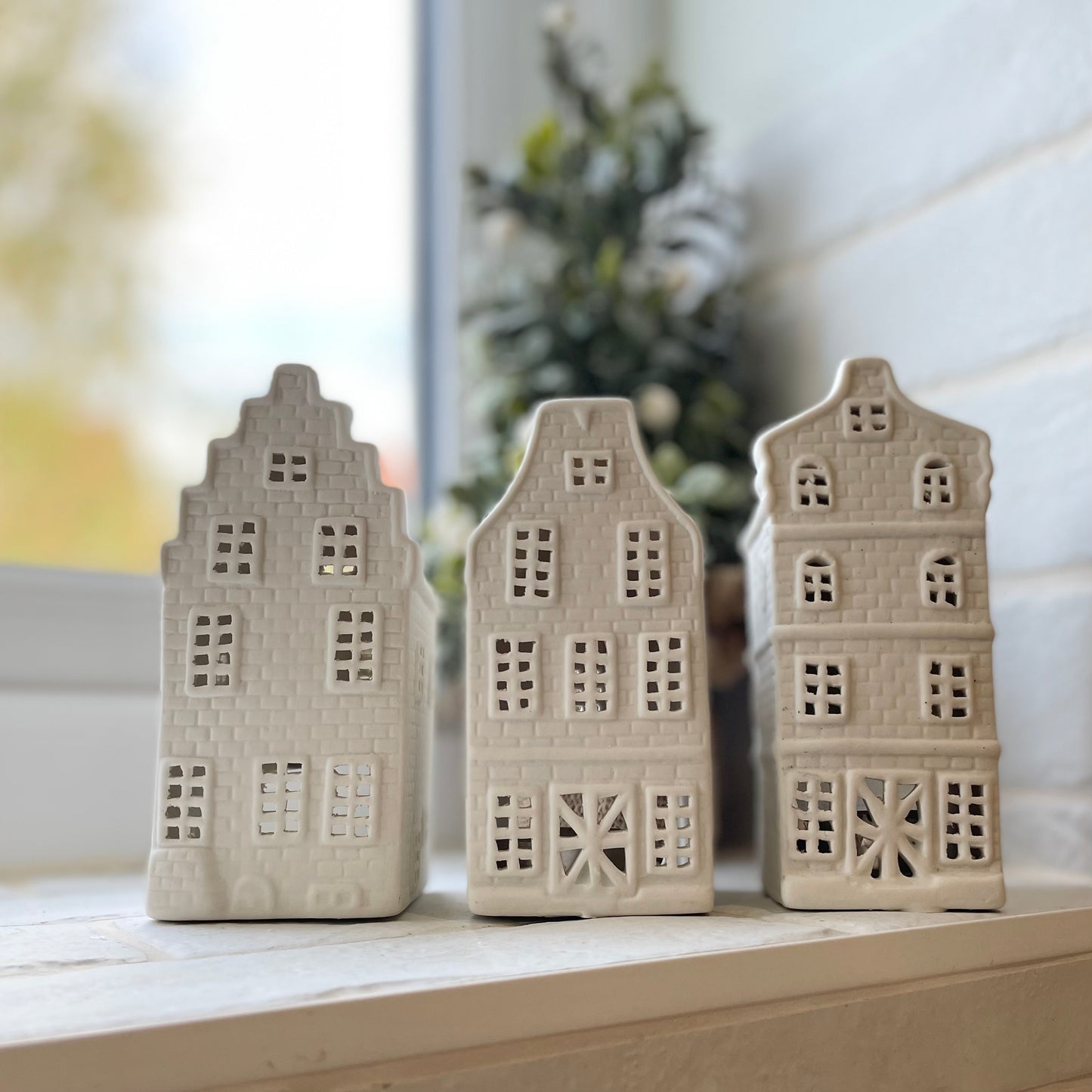 White porcelain canal houses with tiny windows and brick detailing, glowing softly with tea lights on a tiled windowsill.