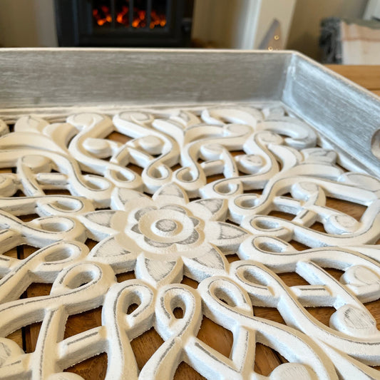 Whitewashed carved wooden tray with distressed finish and side handles, styled with candles and neutral decor on a wooden table.