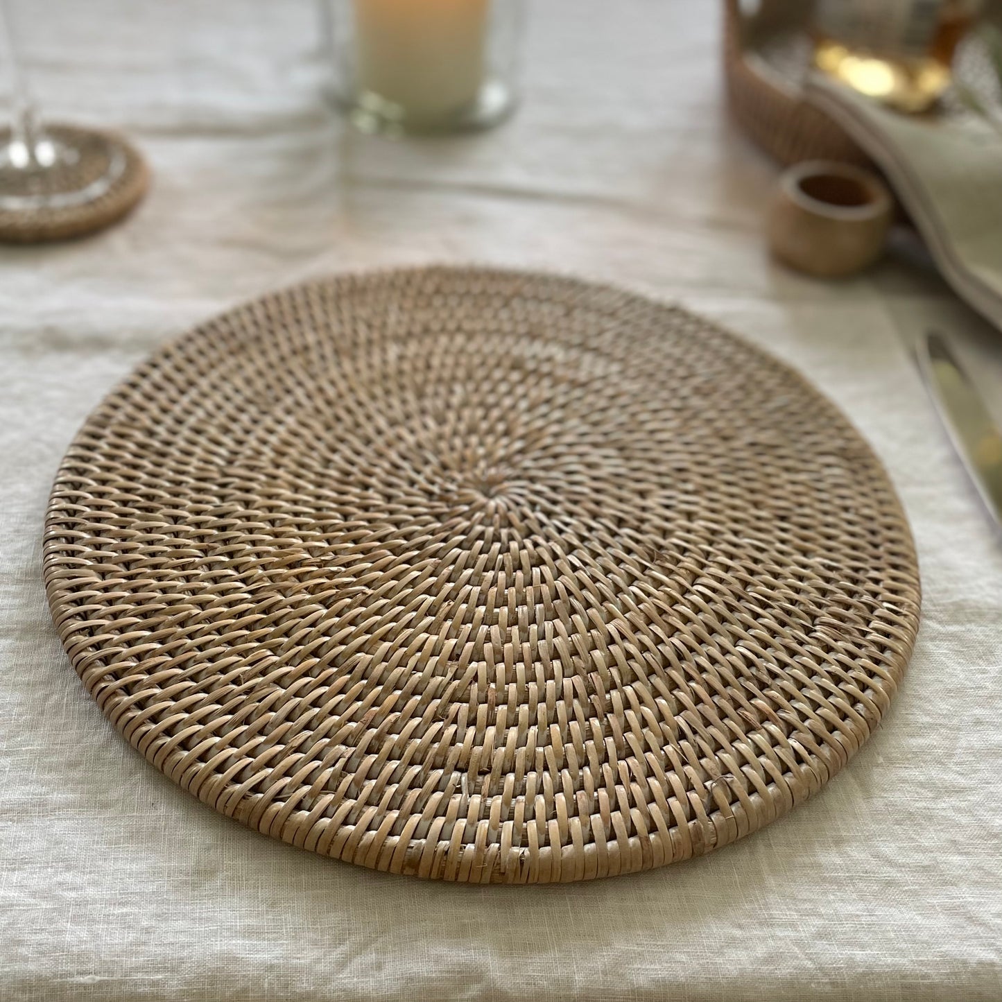 whitewashed rattan round placemat styled on a white linen table setting with rattan coaster.