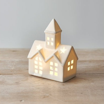 Small white ceramic church ornament with pointed steeple and warm LED light, styled on a festive mantel.
